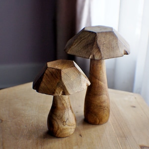 May include: Two wooden mushroom sculptures, one larger than the other, with a geometric design. The mushrooms are a light brown colour and have a smooth finish.