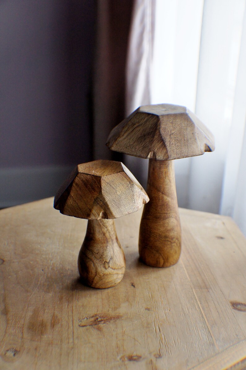 May include: Two wooden mushroom sculptures, one larger than the other, with a geometric design. The mushrooms are a light brown colour and have a smooth finish.