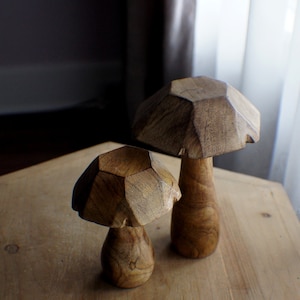 May include: Two wooden mushroom sculptures with a geometric design. The larger mushroom is brown and the smaller mushroom is a lighter brown.