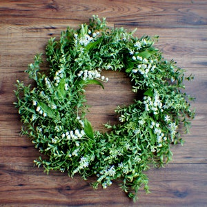 May include: A green wreath with white flowers. The wreath is made of artificial greenery and has a natural look.