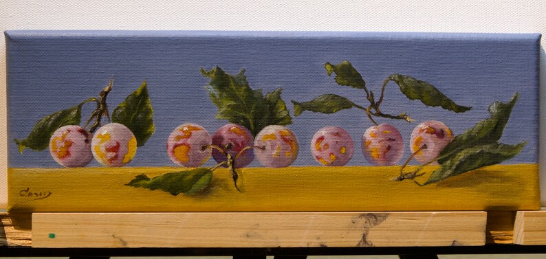 May include: A painting of a still life featuring six plums with pink and purple hues, arranged in a row on a yellow surface. The plums are surrounded by green leaves and branches against a light blue background.