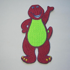 Puede incluir: Parche bordado rojo y verde de un dinosaurio de dibujos animados con una sonrisa de dientes y un brazo levantado.