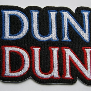 May include: A black fabric patch with the word "DUN" in white, blue, and red lettering, stacked on top of the same word in red, white, and black lettering.