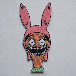 Pode incluir: Orelhas de coelho rosa com um rosto de desenho animado com um sorriso largo e olhos grandes. O rosto é marrom com uma camisa verde.