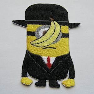 May include: An embroidered patch of a yellow minion wearing a black suit and a black hat with a banana covering one eye.