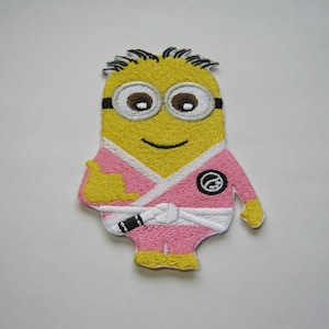 Puede incluir: Parche bordado para planchar con un minion amarillo que lleva un uniforme de karate rosa con cinturón blanco y un círculo negro en el pecho.
