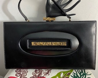 May include: A black leather clutch purse with a gold-toned clasp and a decorative cutout design. The purse has a top handle.
