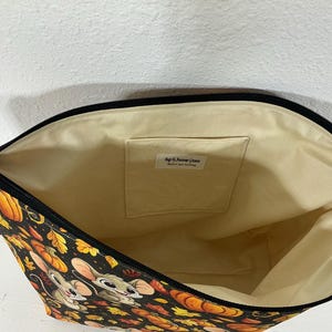 May include: A zippered pouch with a black exterior featuring a pattern of cartoon mice, orange pumpkins, and autumn leaves. The interior is lined with cream-colored fabric and includes an internal pocket with a label reading Bags by Awesome Granny.