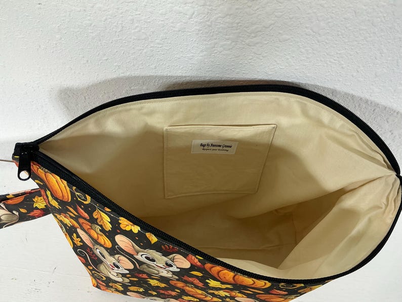 May include: A zippered pouch with a black exterior featuring a pattern of cartoon mice, orange pumpkins, and autumn leaves. The interior is lined with cream-colored fabric and includes an internal pocket with a label reading Bags by Awesome Granny.
