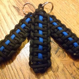 May include: Three black and blue paracord keychains with a silver key ring. The keychains are woven with a thin blue stripe in the center.