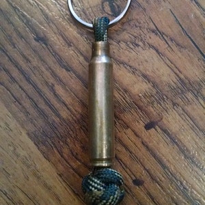 May include: A brass bullet casing keychain with a black, green, and tan paracord knot.