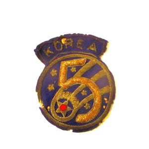 May include: A vintage blue and gold embroidered patch with the word "KOREA" at the top. The patch features a gold "50" design, stars, and a red center. The patch is likely a commemorative item.