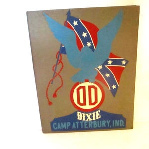 May include: A vintage, rectangular sign with a gray background. It features a blue dove with outstretched wings, two Confederate flags, and a red and white emblem with the letters "OD." The text "Dixie Camp Atterbury, Ind." is at the bottom.