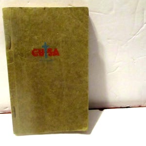 May include: A vintage olive-green book with the red text "EUSA" and a blue cross symbol. The book has a textured cover and appears to be bound with staples. The background is a white surface.