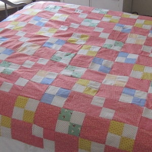 Puede incluir: Una colcha de retazos con un patrón de cuadros en tonos de rosa, amarillo, azul y blanco.