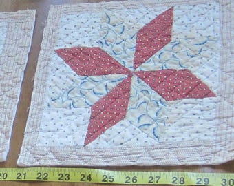 Op de afbeelding: Een vierkant gewatteerd stoffen blok met een centraal sterpatroon van rode stof met witte stippen en crèmekleurige stof met blauwe bladmotieven. Een geel meetlint toont een breedte van ongeveer 21,5 cm.