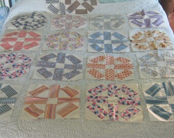Op de afbeelding: Een verzameling van zestien vierkante quiltblokken gerangschikt in een raster, elk met een centraal wit vierkant omringd door vier rechthoekige stoffen stukken met diverse patronen, waaronder strepen, bloemen en ruitjes.