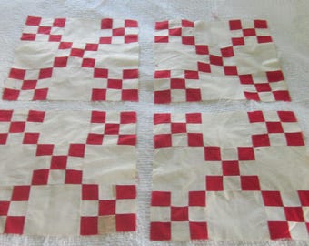 Op de afbeelding: Vier vierkante quiltblokken van stof met een rood-wit dambordpatroon. Elk blok is opgebouwd uit kleinere rode en witte vierkantjes die in een raster zijn gerangschikt, wat zorgt voor een herhalend geometrisch ontwerp op alle vier de stukken stof.