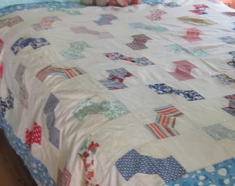 Op de afbeelding: Een patchwork quilt met een witte achtergrond en verspreide, veelkleurige stoffen blokken in diverse patronen, waaronder strepen, bloemen en geometrische vormen. De quilt is afgewerkt met een blauw-witte rand met een patroon langs de zijkanten.