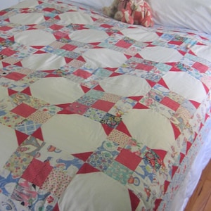 May include: A white bed with a red and white patchwork quilt. Two teddy bears are sitting on the bed.