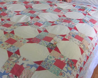 Puede incluir: Una cama blanca con una colcha de retazos roja y blanca. Dos ositos de peluche están sentados en la cama.