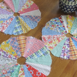 May include: Three circular fabric fan shapes constructed from multiple pieced wedges of assorted vintage cotton prints. Each piece features a variety of colorful patterns including floral, plaid, gingham, and polka dot designs in red, blue, yellow, and green.