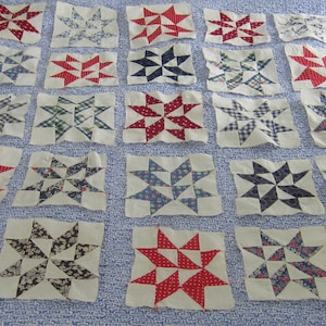 Pode incluir: Uma coleção de blocos de colcha em forma de estrela em várias cores e padrões. Os blocos apresentam estrelas vermelhas, azuis e pretas sobre um fundo branco. Os padrões de tecido incluem bolinhas, xadrez e desenhos florais.