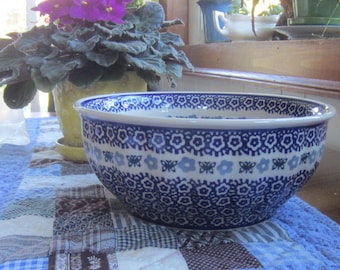 Op de afbeelding: Een keramische kom met een witte basis en een herhalend patroon van donkerblauwe bloemen, lichtblauwe bloemen en kleine donkerblauwe vlinders. De kom heeft een brede, ronde opening en een gladde, geglazuurde afwerking in een blauw-wit kleurenschema.
