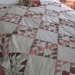 May include: A white quilt with a patchwork design featuring red and brown triangles. Two stuffed animals, a brown bear and a red fox, are sitting on the quilt.