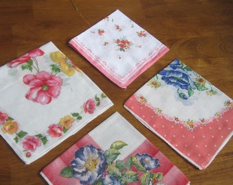 Op de afbeelding: Vier vierkante zakdoeken met bloemmotieven. Eén heeft roze en gele bloemen, een andere heeft kleine rode bloemtrossen met een roze rand, één heeft blauwe bloemen met een roze stippenrand en één heeft blauwe bloemen op een rode ruitjesachtergrond.