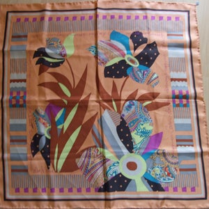 May include: A peach-colored silk scarf with a colorful floral design. The design features brown leaves, blue, pink, and green flowers, and a paisley pattern.