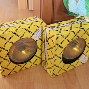 May include: Two yellow round car headlights with black housings and CIBIE 165 printed on the yellow boxes they are packaged in.