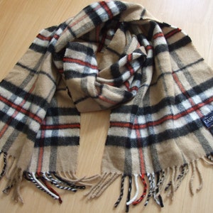 May include: A tan and black plaid scarf with fringe. The scarf has a label that reads "The Cashmere Store 100% Cashmere Made in Scotland".