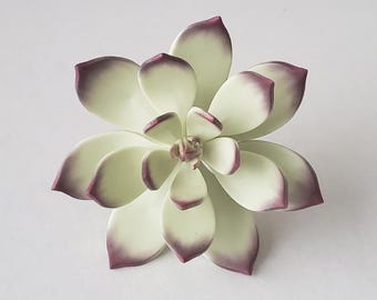 May include: A decorative succulent ornament featuring layered, smooth petals in a pale, creamy off-white color. Each petal is tipped with a distinct, deep purple gradient that transitions from the edges toward the center of the plant structure.