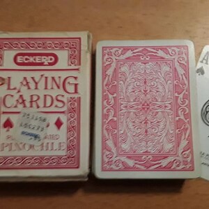 Puede incluir: Una baraja de cartas Eckerd con un diseño rojo y blanco. La caja dice "Playing Cards" y "Pinochle". El dorso de las cartas tiene un diseño floral rojo y blanco. También se muestra el as de picas.