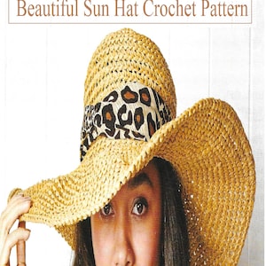 May include: A wide-brimmed straw sun hat with a leopard print ribbon. The hat is crocheted and has a brown and black colour scheme. The hat is being worn by a person with long brown hair.