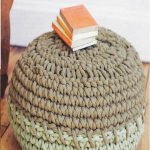 May include: A brown and green crocheted pouffe with a stack of books on top. The pouffe is made with a thick, chunky yarn and has a simple, modern design.