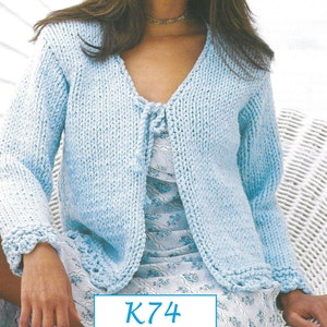 Puede incluir: Un cárdigan de punto azul claro con un cierre de nudo en la parte delantera y mangas largas. El cárdigan se muestra en una modelo que lleva un vestido floral. El texto "K74" es visible en la parte inferior de la imagen.