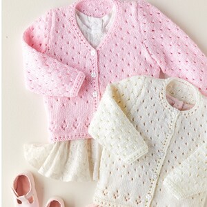 May include: Two knitted baby cardigans, one pink and one white, with a button closure and a delicate lace pattern. The cardigans are laid out on a white background with a number "318" visible in the lower left corner.