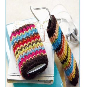 May include: Two colorful knitted phone and iPod covers with a brown base and multi-colored stripes. The covers are on top of a stack of books with a blue cover on top. The text "KA4" is on a white oval in the bottom center of the image.