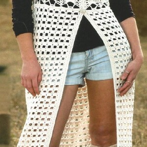 Puede incluir: Chaleco largo de crochet blanco con frente abierto y cierre de botones. El chaleco presenta una mezcla de patrones calados y se usa sobre una camiseta negra y pantalones cortos de mezclilla. La imagen incluye el texto "AD18" en un cuadro azul.