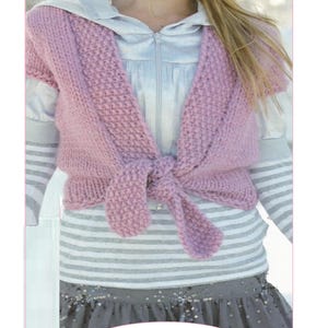 May include: A pink knit tie-front cardigan with a textured stitch pattern, worn over a light gray zip-up hoodie and a gray skirt with sequins. The image includes the text Tie Front Cardigan Knitting Pattern and the code K43 at the bottom.