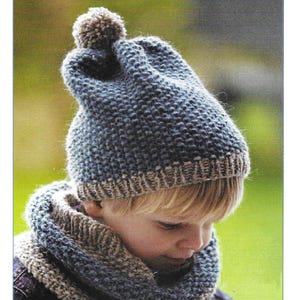 Può includere: Un set di cappello e collo a maglia blu e marrone con un pon pon sulla cima del cappello. Il set è etichettato "C13".