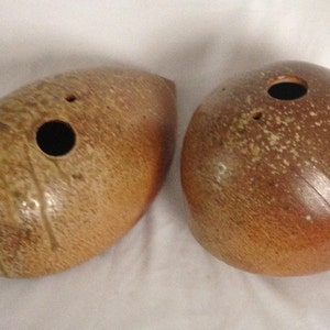 May include: Two ceramic vases, one with a rounded shape and the other with a more elongated shape. Both vases are brown with a speckled glaze and have a hole at the top for flowers.