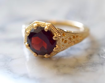 May include: A gold ring with a red gemstone set in a filigree design.