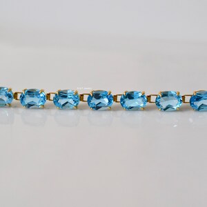 May include: A gold bracelet with oval-shaped blue topaz gemstones. The bracelet has a clasp closure.
