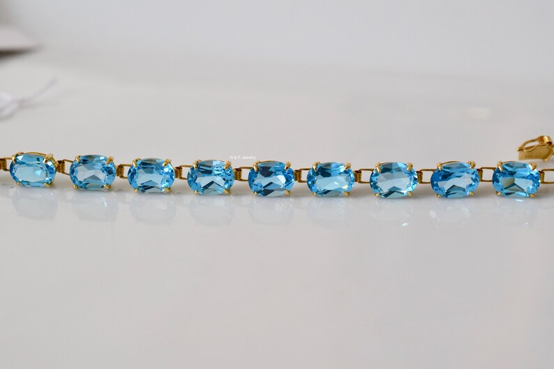 May include: A gold bracelet with oval-shaped blue topaz gemstones. The bracelet has a clasp closure.
