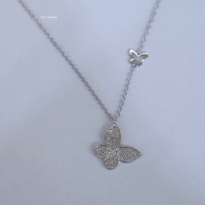 May include: A silver necklace with two butterfly pendants. The larger pendant is covered in small, clear stones. The smaller pendant is plain.