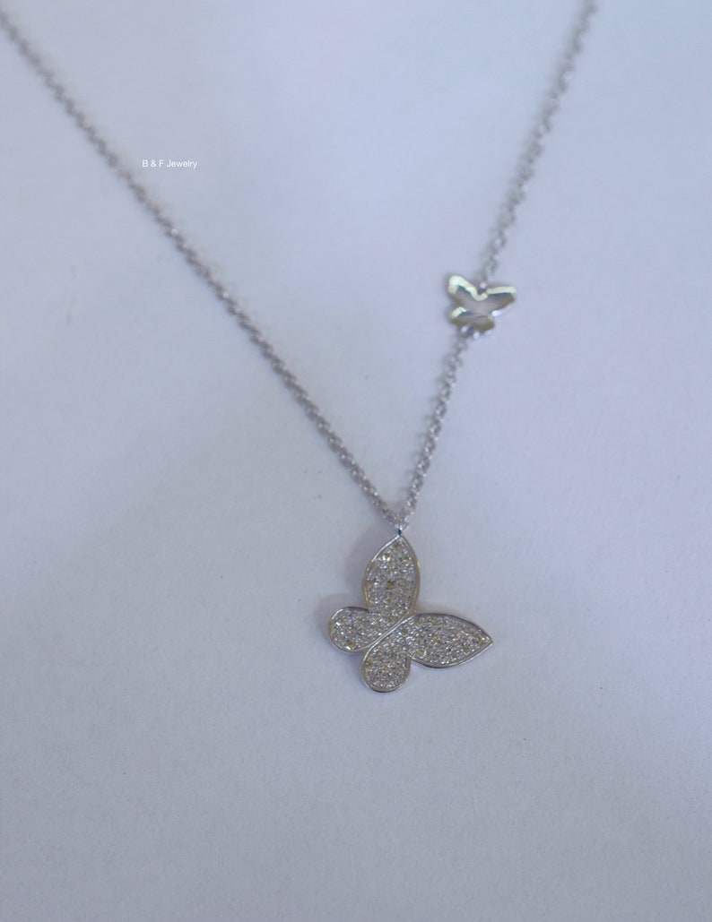 May include: A silver necklace with two butterfly pendants. The larger pendant is covered in small, clear stones. The smaller pendant is plain.
