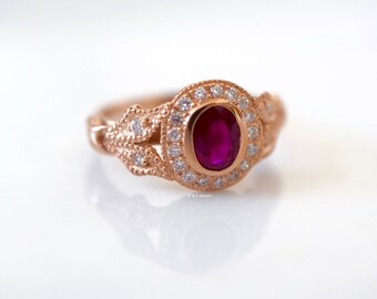 May include: A rose gold ring with a ruby gemstone surrounded by a halo of smaller diamonds. The ring has a delicate, intricate design.